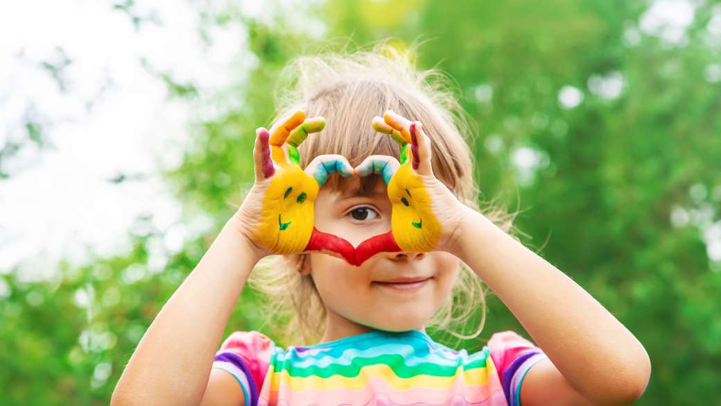 Child with paint on his hand showing a heart with her hands