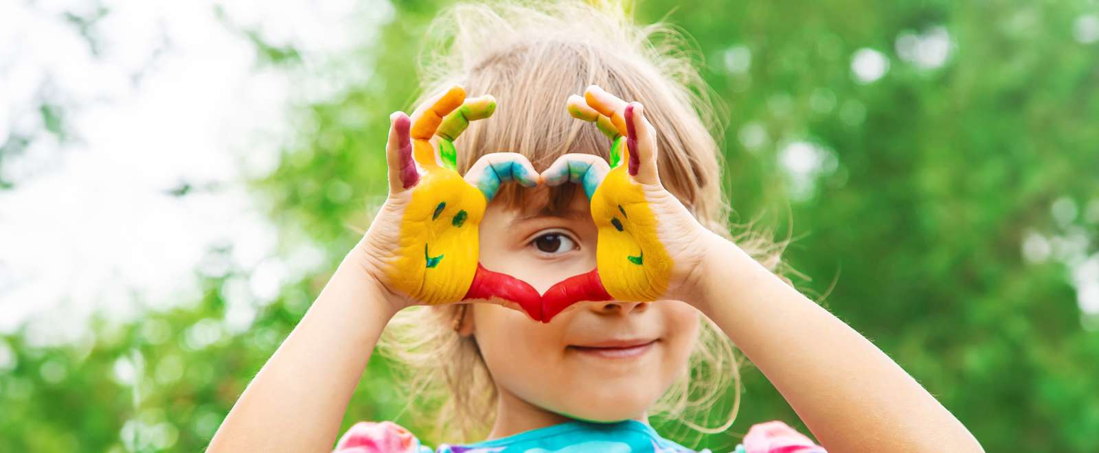 Child with paint on his hand showing a heart with her hands